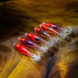 Multi color mini transparent shrimp squid jig collection with red cloth head and crown hooks on wooden background