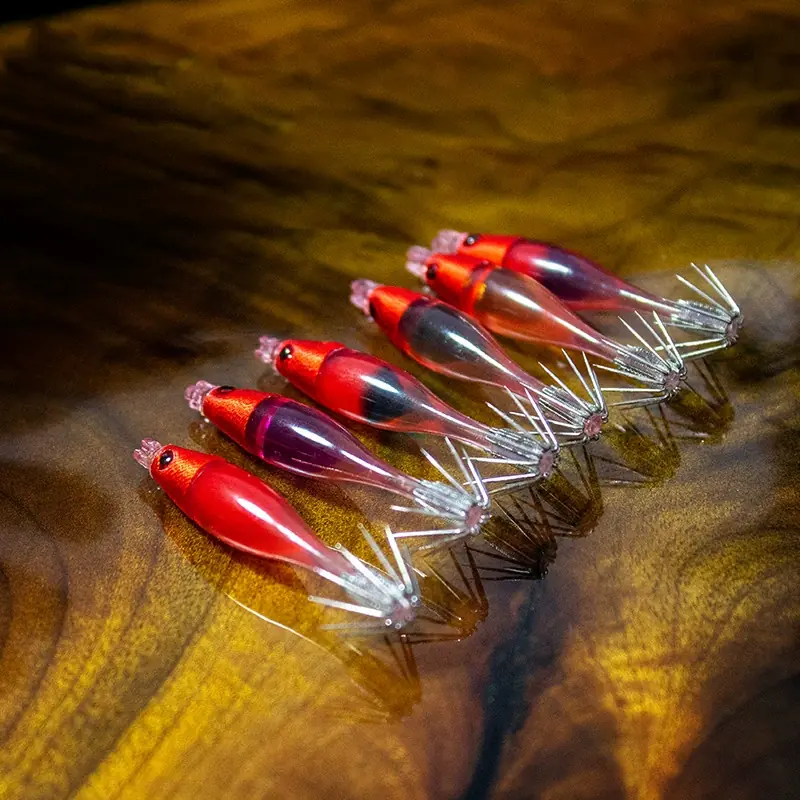 Multi color mini transparent shrimp squid jig collection with red cloth head and crown hooks on wooden background