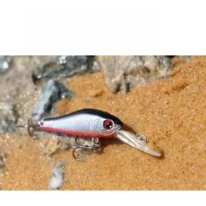 Micro deep diving minnow trout lure resting on sandy stream bank outdoors